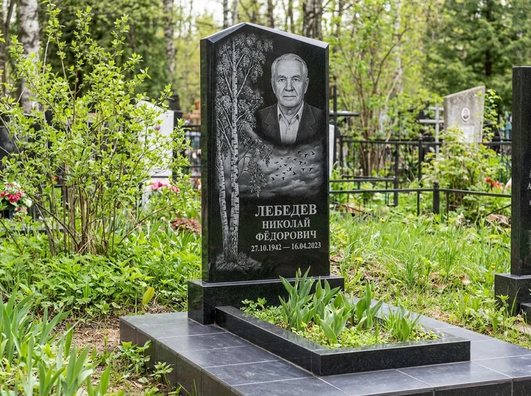 Памятник с гравировкой берёзы: вертикальная стела со скошенным верхом — берёза и стая птиц в небе, гранитный цоколь с тёмной плиткой, работа «Лебедев» в Магнитогорске