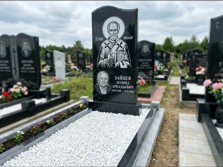 Памятник с гравировкой иконы: стела с крестообразным навершием — икона в резной рамке-киоте, газон без ограды, стриженая трава, работа «Раевская» в Магнитогорске