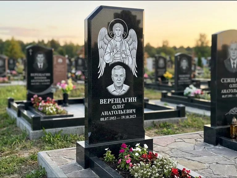 Памятник с гравировкой иконы: стела с резным навершием и нимбом в золоте — гравировка образа Спасителя, высокие разросшиеся туи полукругом, работа «Мельникова» в Магнитогорске