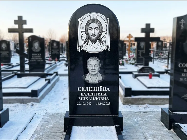 Памятник с гравировкой иконы: небольшая скромная одиночная стела с именной иконой — золочёный нимб на образе, аккуратный участок с газоном, работа «Ковалёв» в Магнитогорске