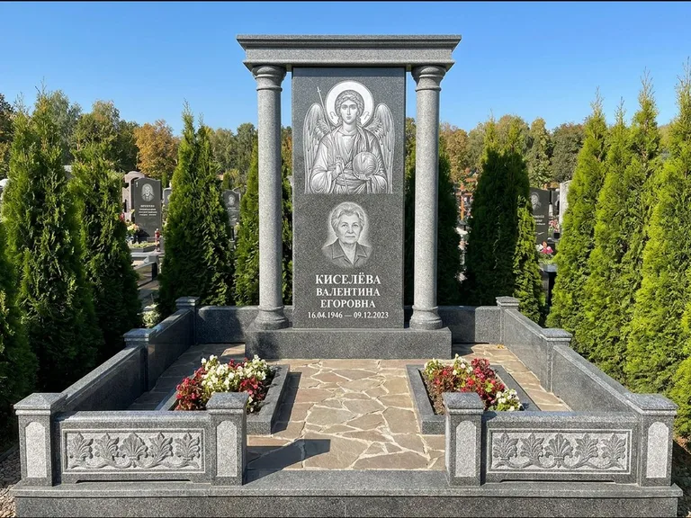 Памятник с гравировкой иконы: массивная стела с двускатным навершием-домиком — гравировка Николая Чудотворца, живая изгородь из туи, работа «Журавлёв» в Магнитогорске