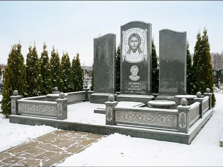 Памятник с гравировкой иконы: узкая вертикальная стела-пилон с ликом — икона в резной рамке-киоте, открытая лужайка без ограды, работа «Одинцов» в Магнитогорске