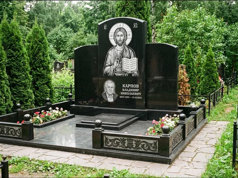 Памятник с гравировкой иконы: широкая панорамная стела с золочёным нимбом — гравировка образа Матроны Московской, цветник с белыми хризантемами, работа «Мельникова» в Магнитогорске