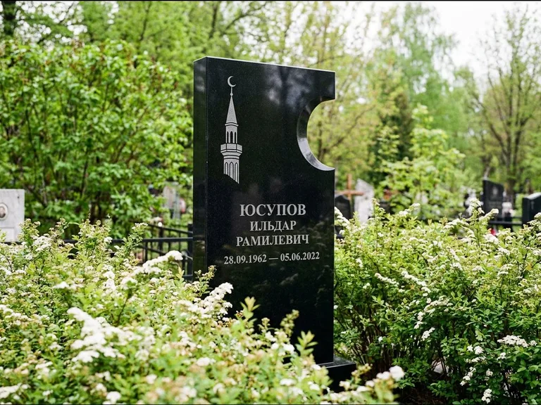 Мусульманский памятник с гравировкой мечети: стела с боковым вырезом в форме полумесяца — гравировка минарета с полумесяцем, низкие кусты спиреи в цвету, работа «Юсупов» в Магнитогорске