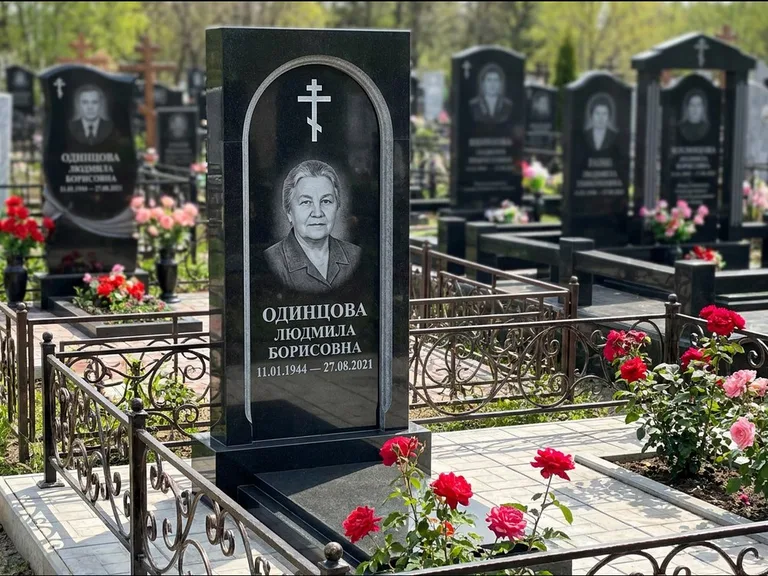 Памятник из чёрного гранита — скромная невысокая стела с крестом с терновым венцом, работа «Лаврентьева» в Магнитогорске
